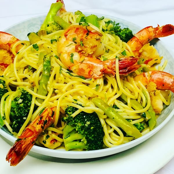 Peruvian spaghetti with shrimp, broccoli, and asparagus, garnished with fresh herbs in a white bowl.