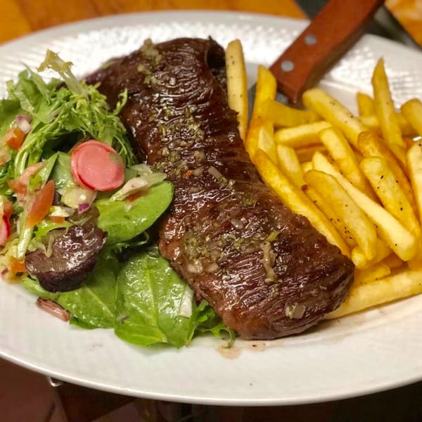Peruvian steak with chimichurri, golden french fries, and a fresh green salad on a white plate.