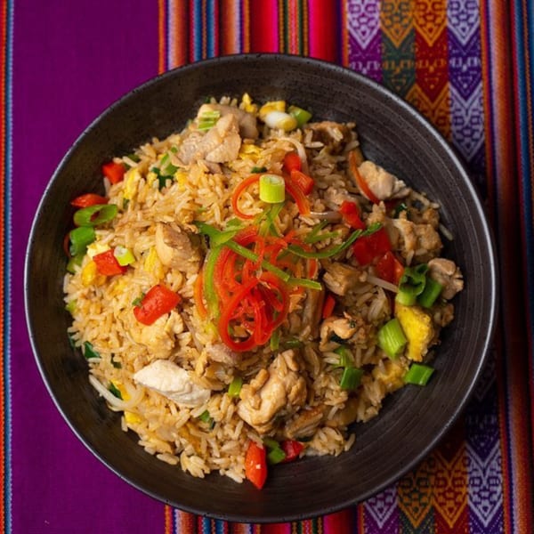 Peruvian arroz chaufa with chicken, red and green peppers, and scallions in a black bowl.