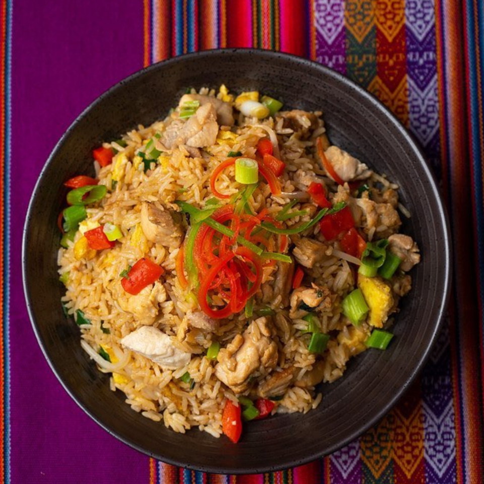 Peruvian arroz chaufa with chicken, red and green peppers, and scallions in a black bowl.