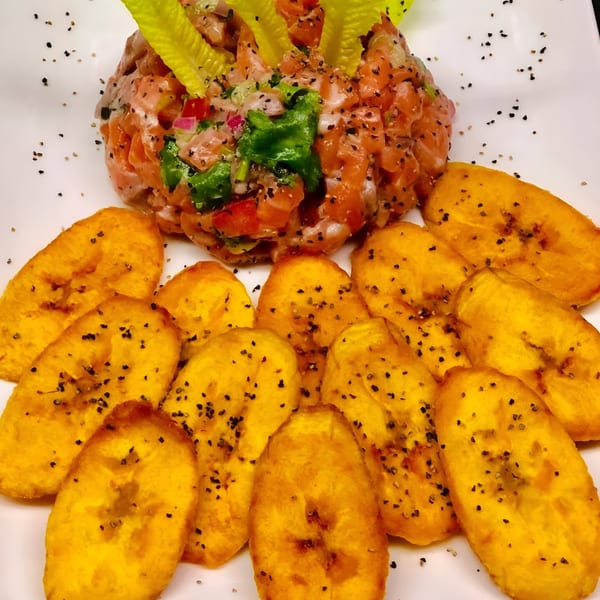 Peruvian salmon ceviche with red onion, cilantro, and fried plantain slices on a white plate.