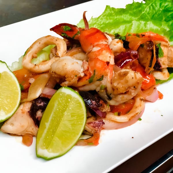 Peruvian seafood dish with shrimp, calamari, octopus, red onions, and lime wedges on a white plate.